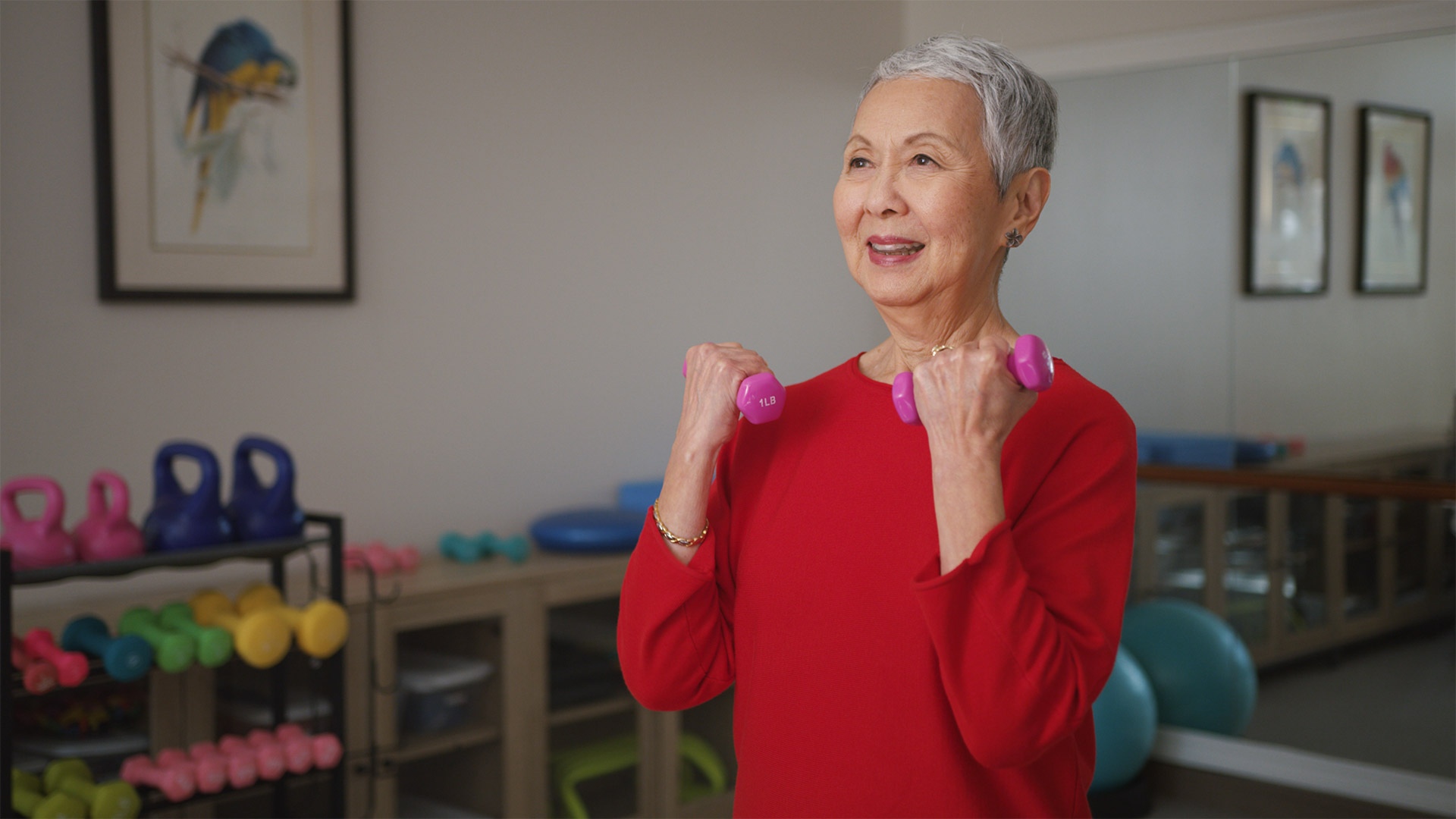 Senior woman in a red shirt exercising with purple dumbbells in a wellness center.
