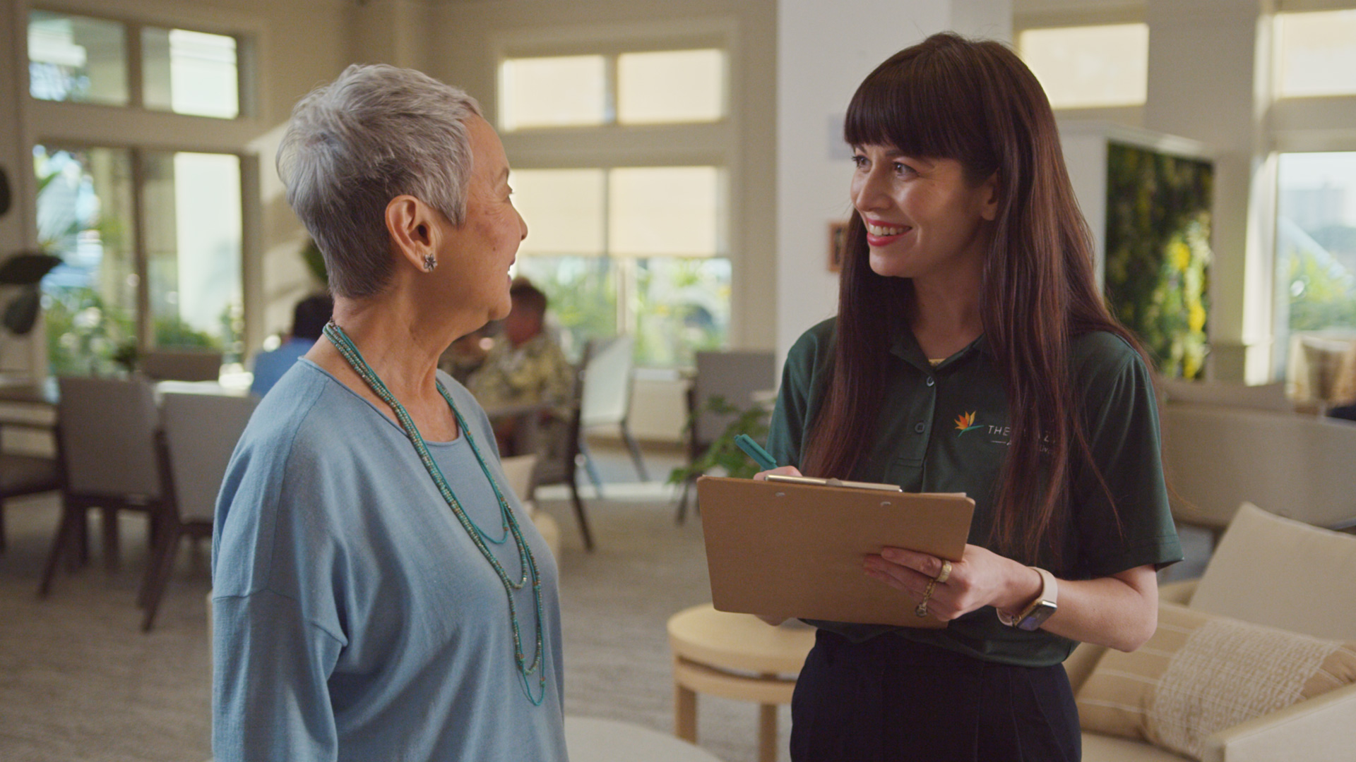 Staff at The Plaza Assisted Living speaking with a resident in a bright common area.