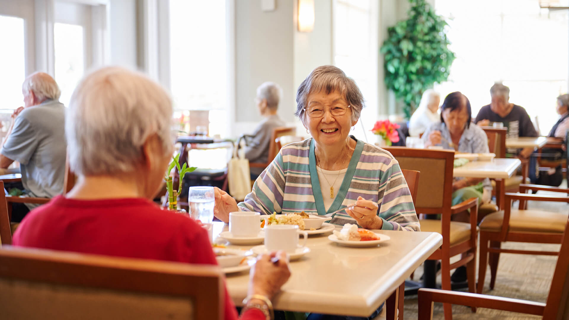 Smiling senior resident enjoying a social meal at The Plaza Assisted Living.
