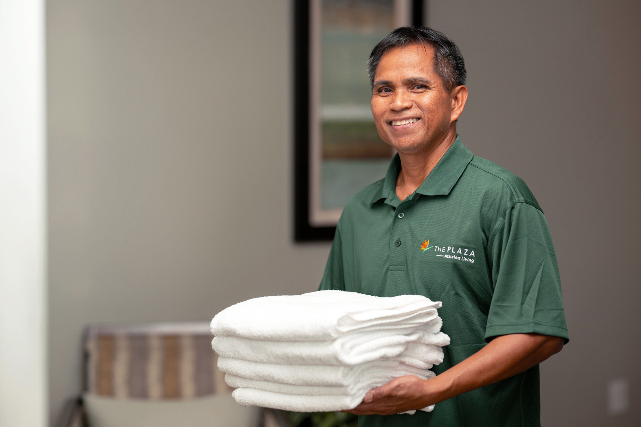 Staff member holding fresh linens at a plaza assisted living location.
