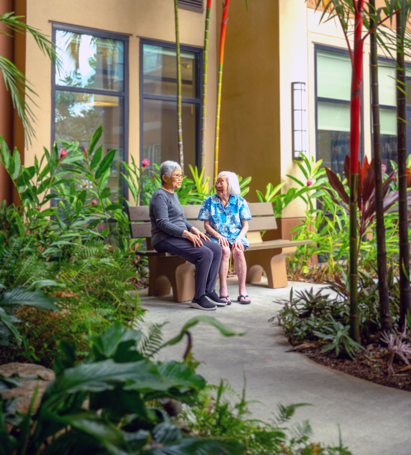 Two women chatting on a bench in the courtyard at Plaza Assisted Living.