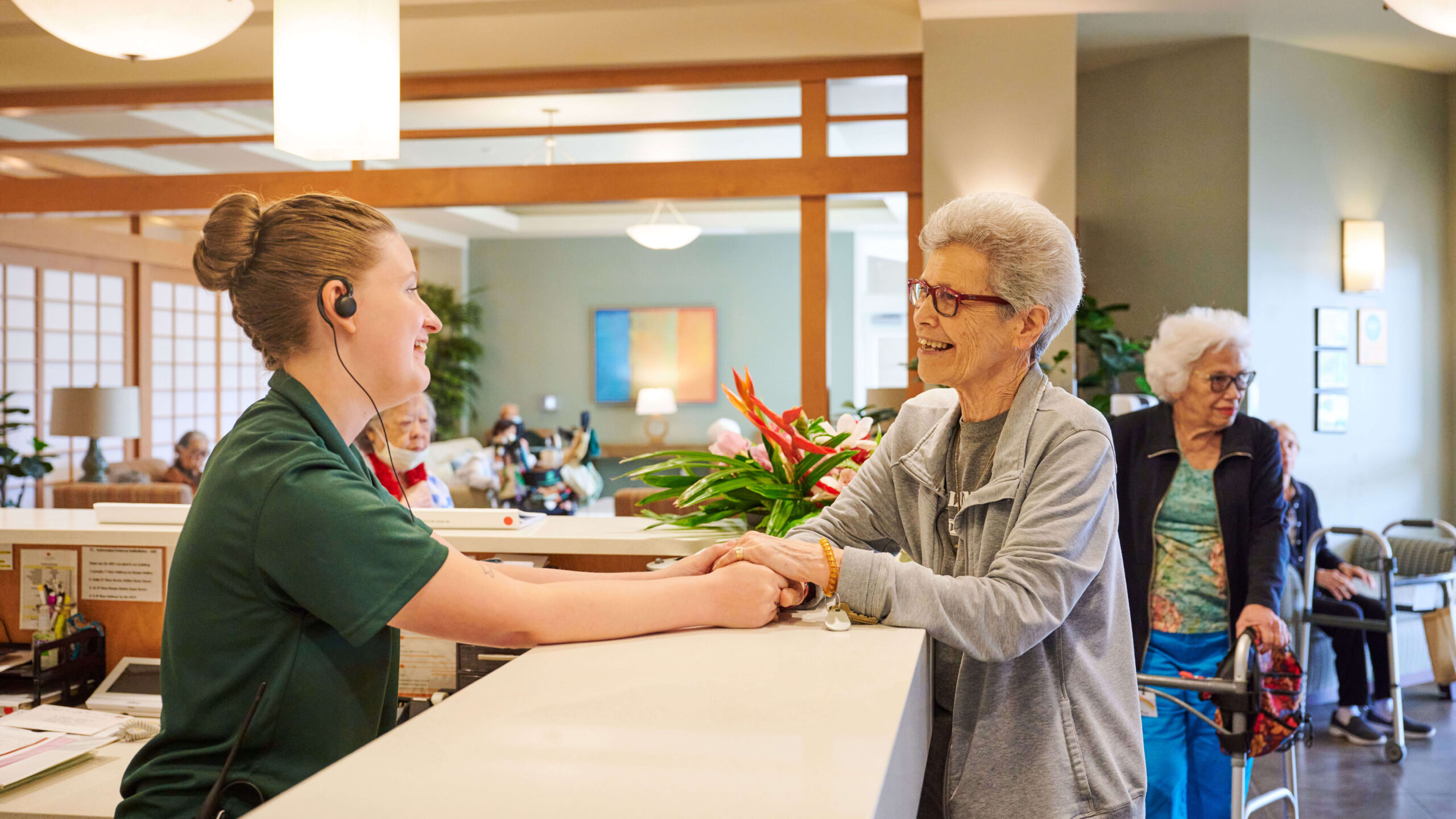 Friendly staff member holding a resident's hand at the reception desk.