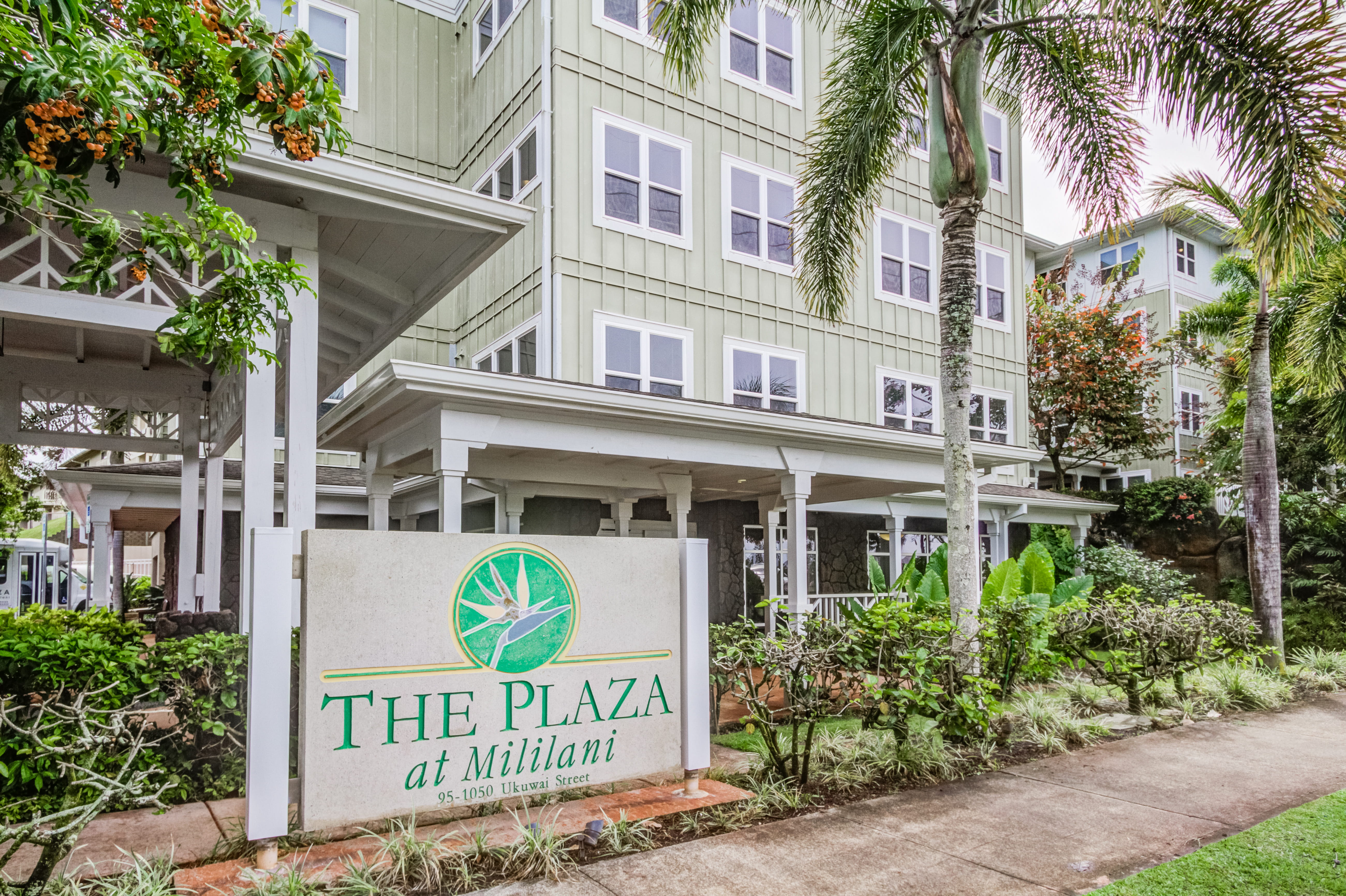 The Plaza at Mililani entrance sign in front of the multi-story senior living building.