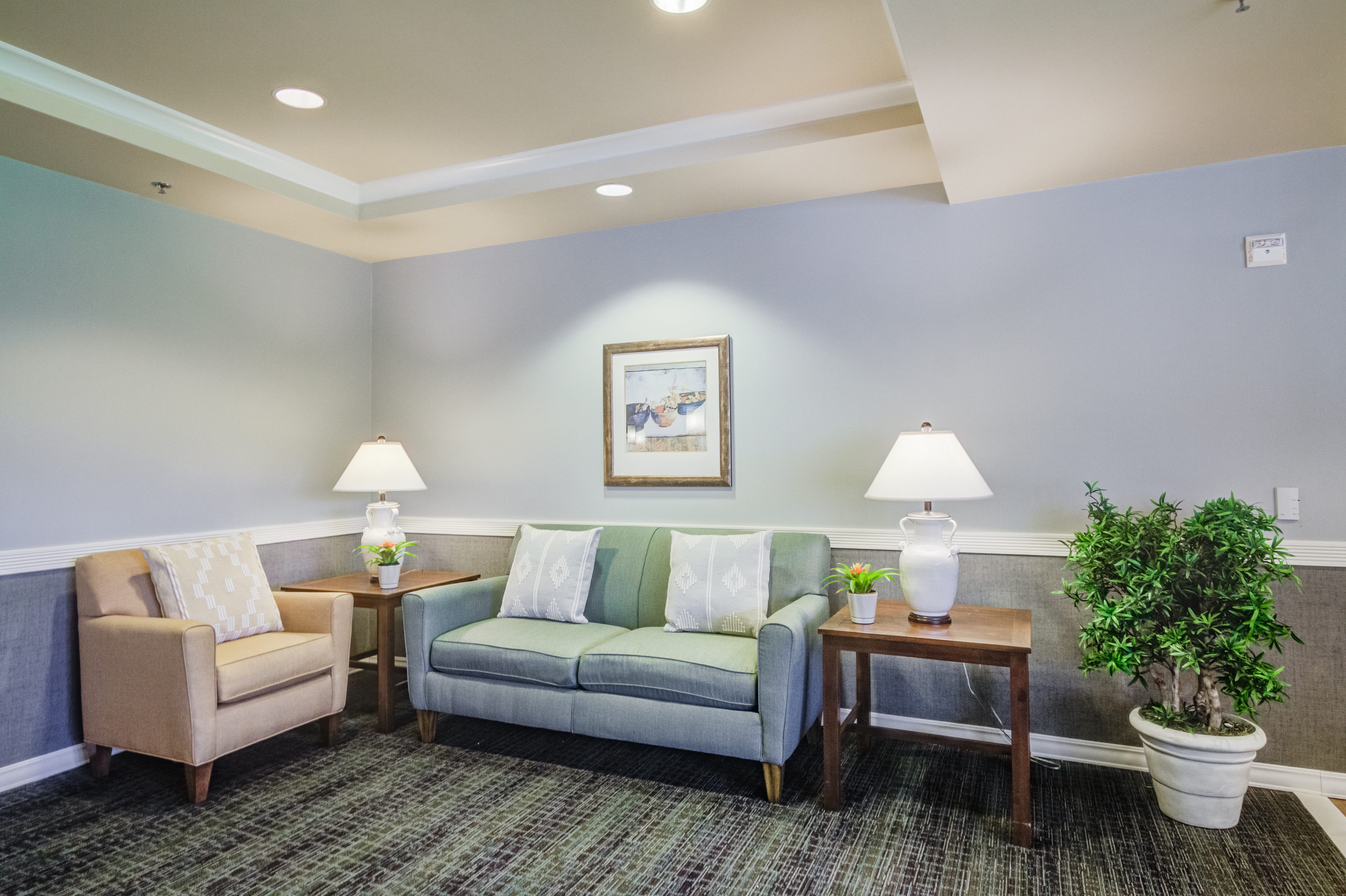 Comfortable lounge with a green sofa and armchair at The Plaza Assisted Living.