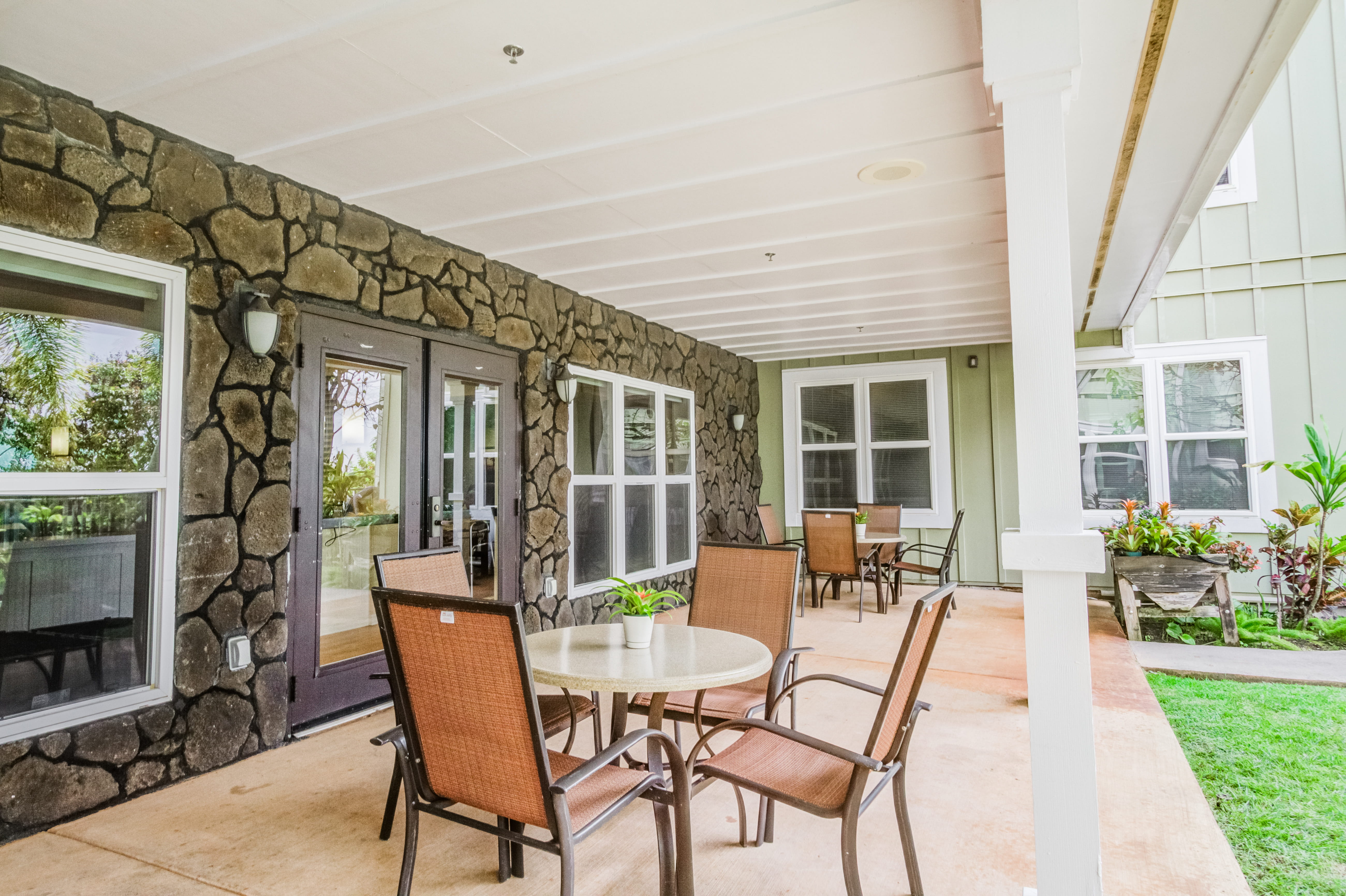 Shaded outdoor lanai with tables and chairs for residents at a local senior living facility.