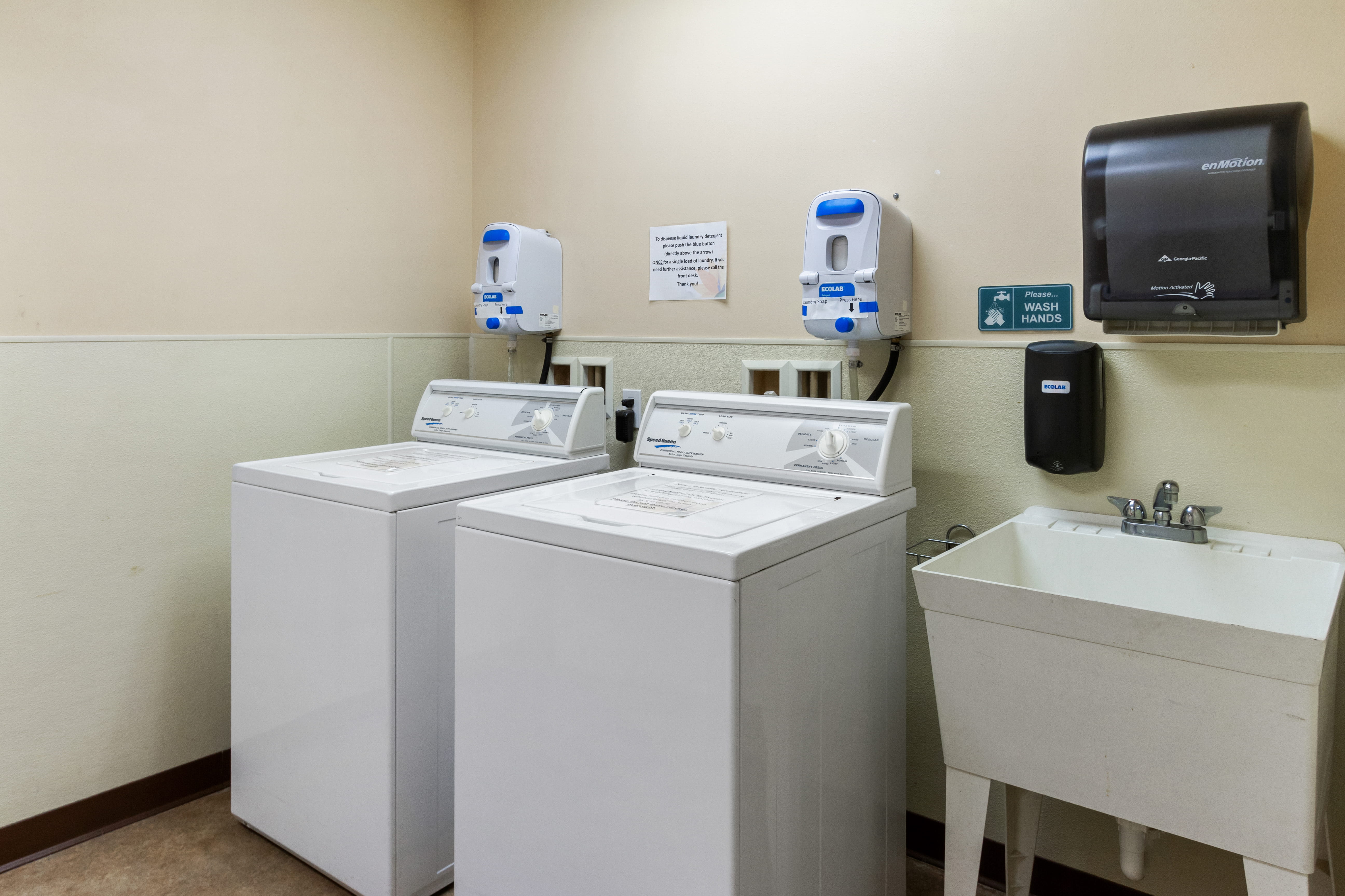 Clean laundry facility with washing machines and a deep sink at The Plaza Assisted Living.