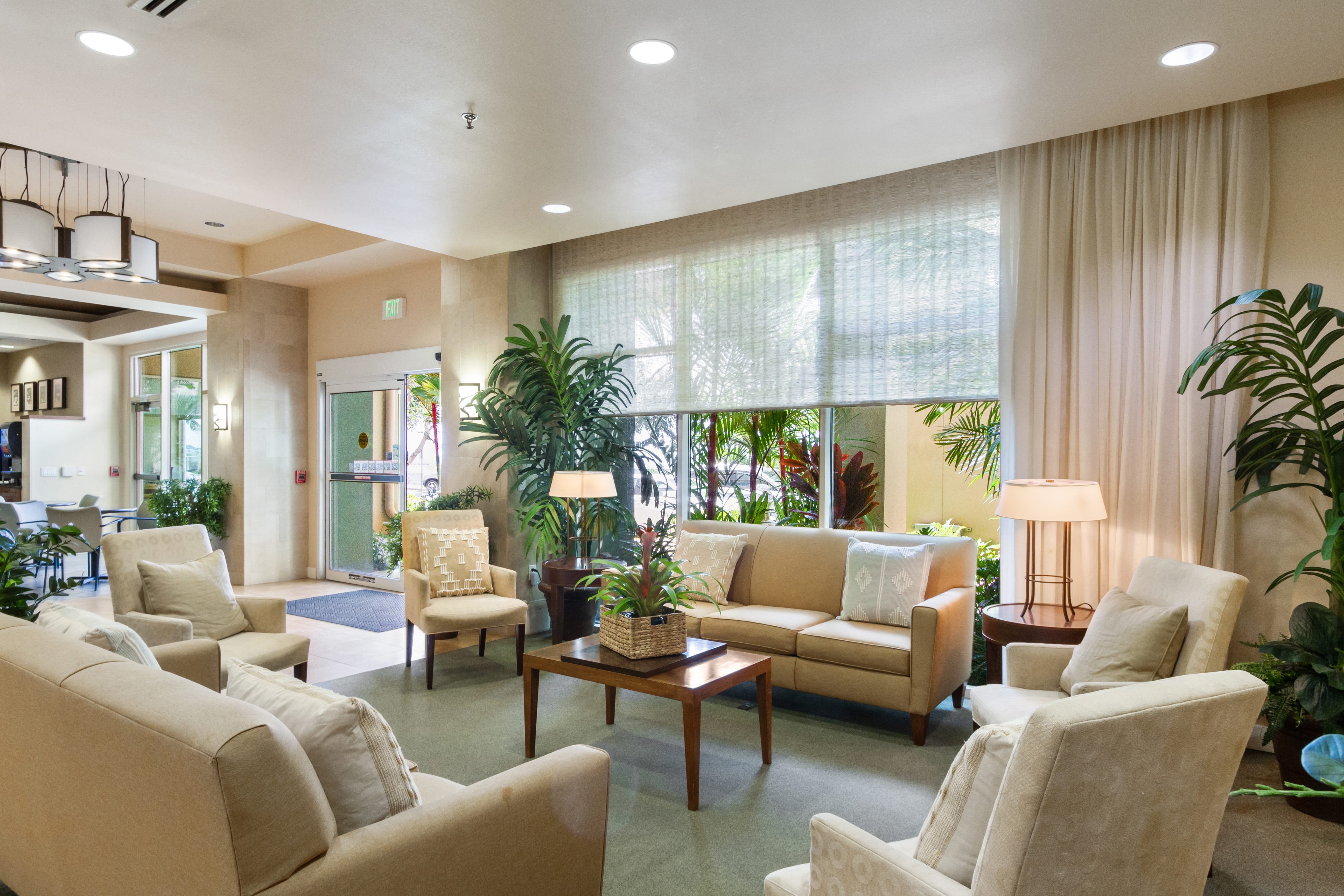 Sunlit lounge area with comfortable sofas and tropical plants at The Plaza Assisted Living.