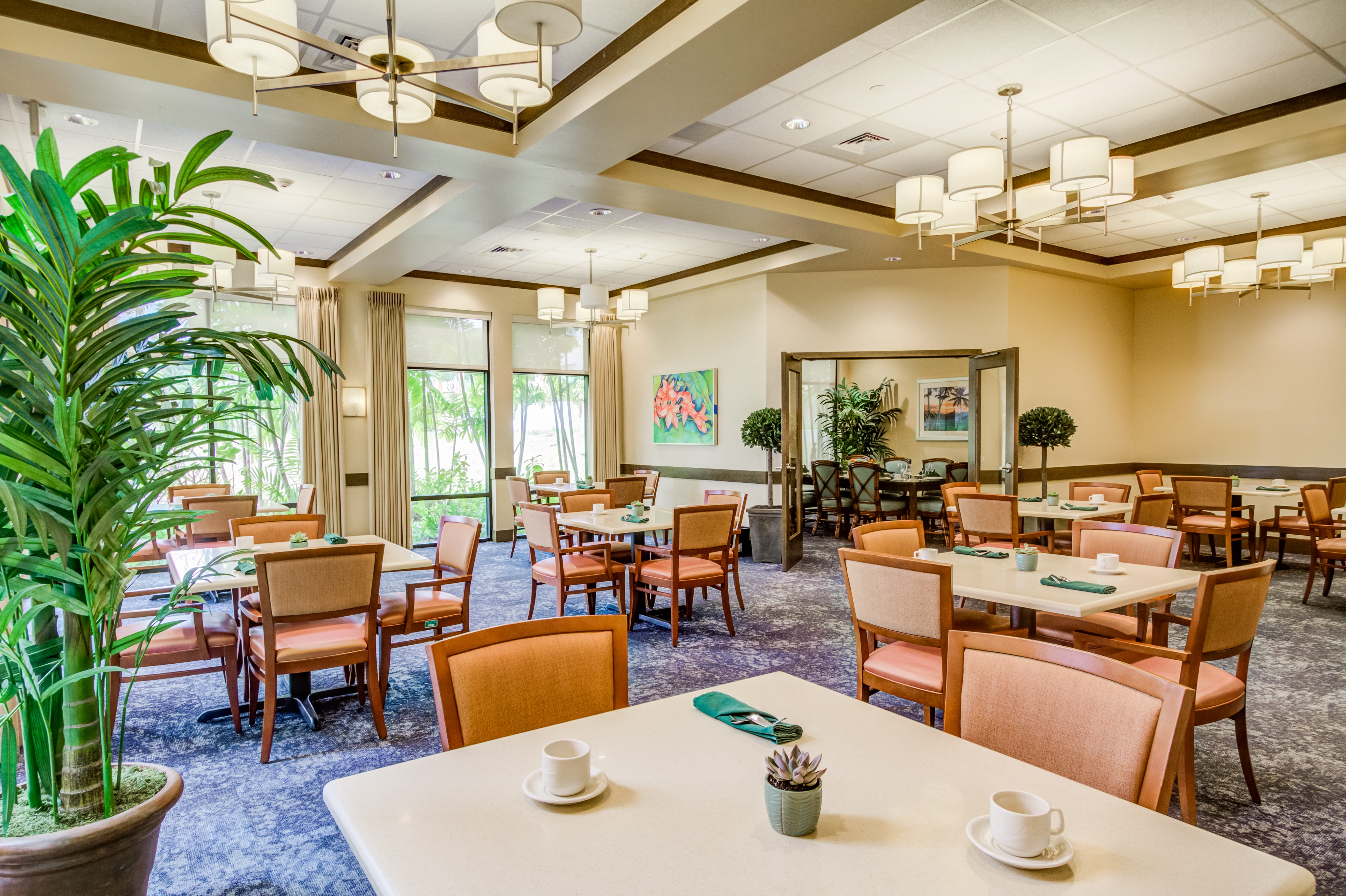 Sunlit dining area at The Plaza Assisted Living with a view of lush greenery.