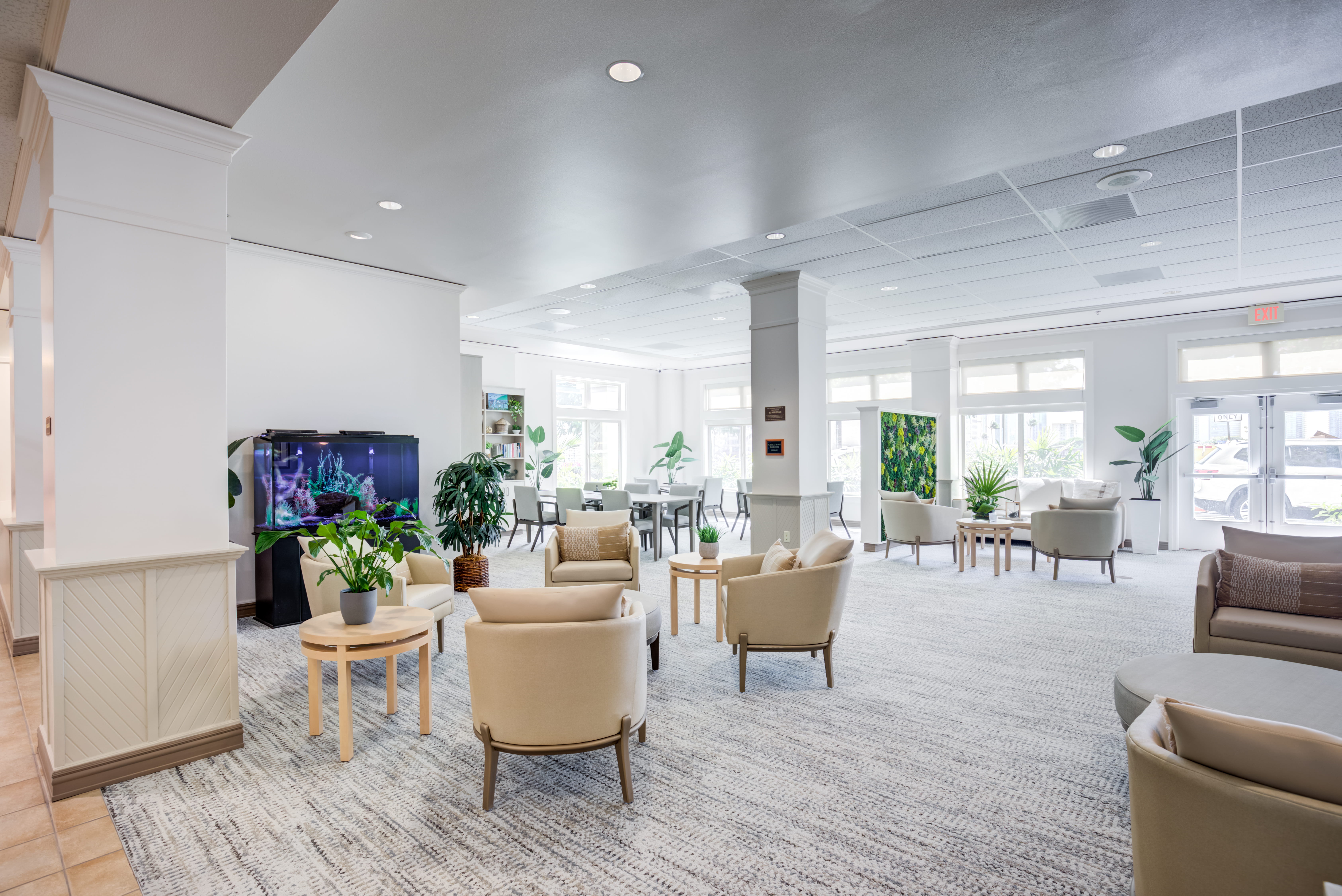 Sunlit lobby lounge with an aquarium and plant wall at The Plaza Assisted Living.