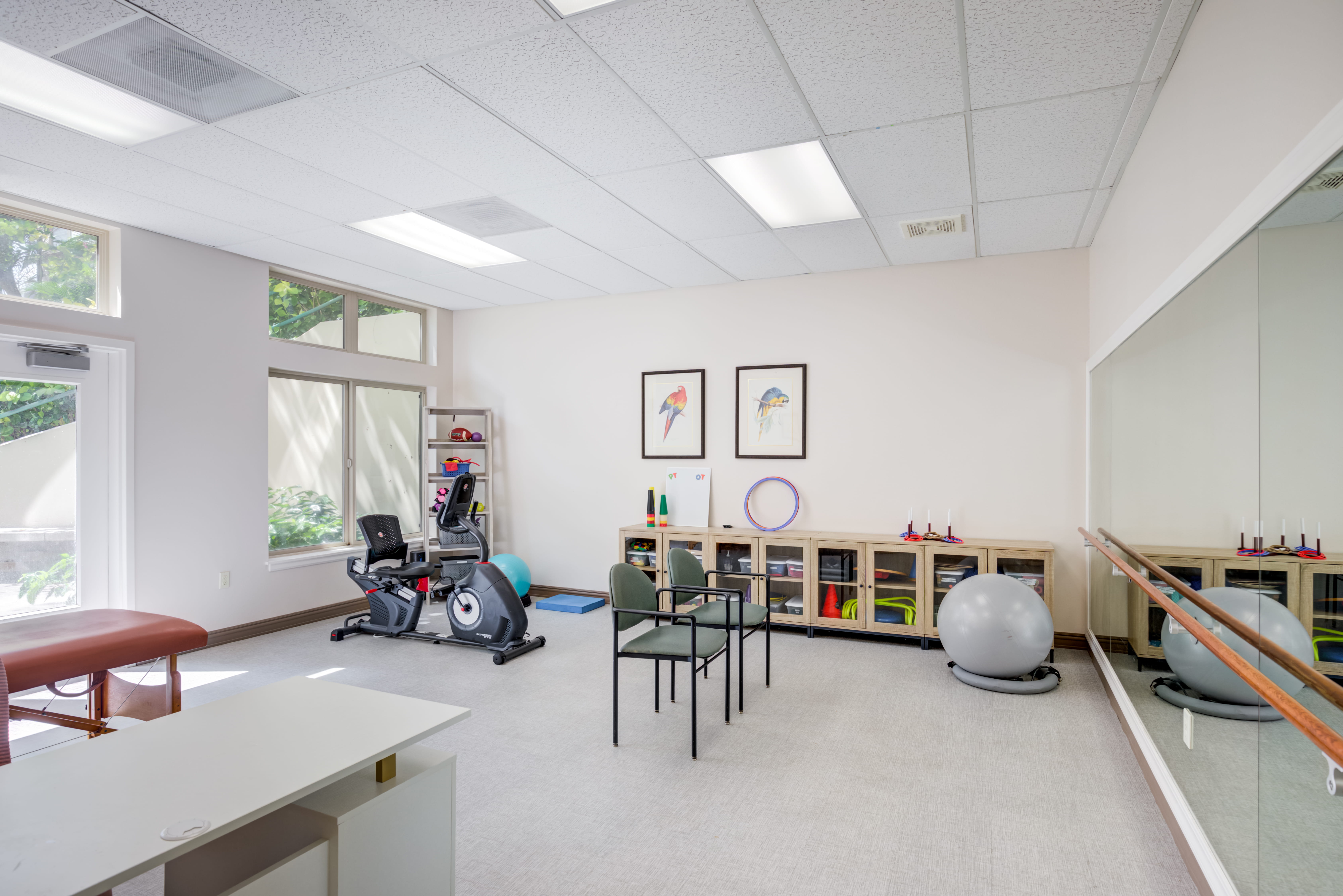 Rehabilitation gym with exercise equipment and a mirror at The Plaza Assisted Living.