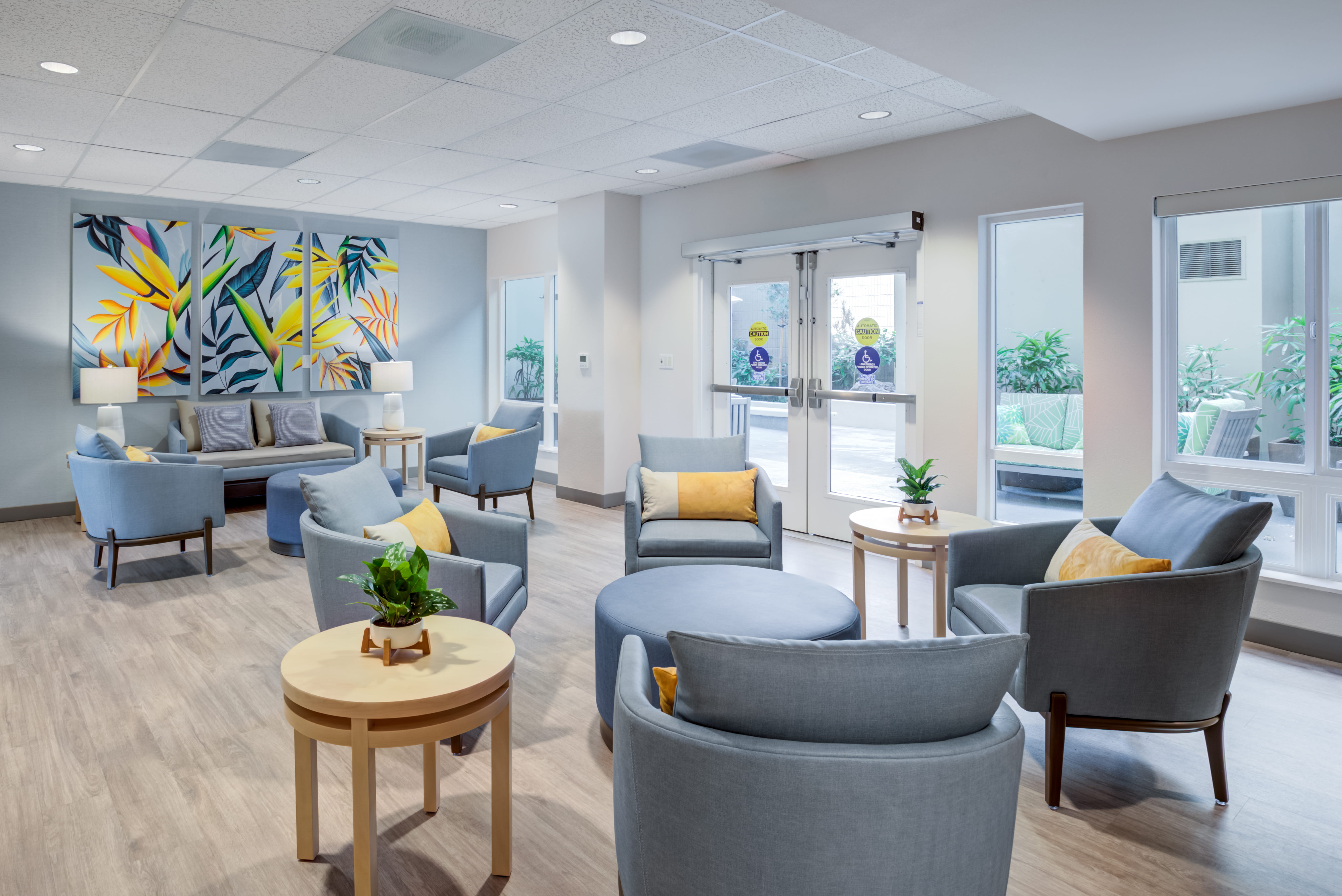 Bright sitting area with blue chairs and tropical artwork at The Plaza Assisted Living.