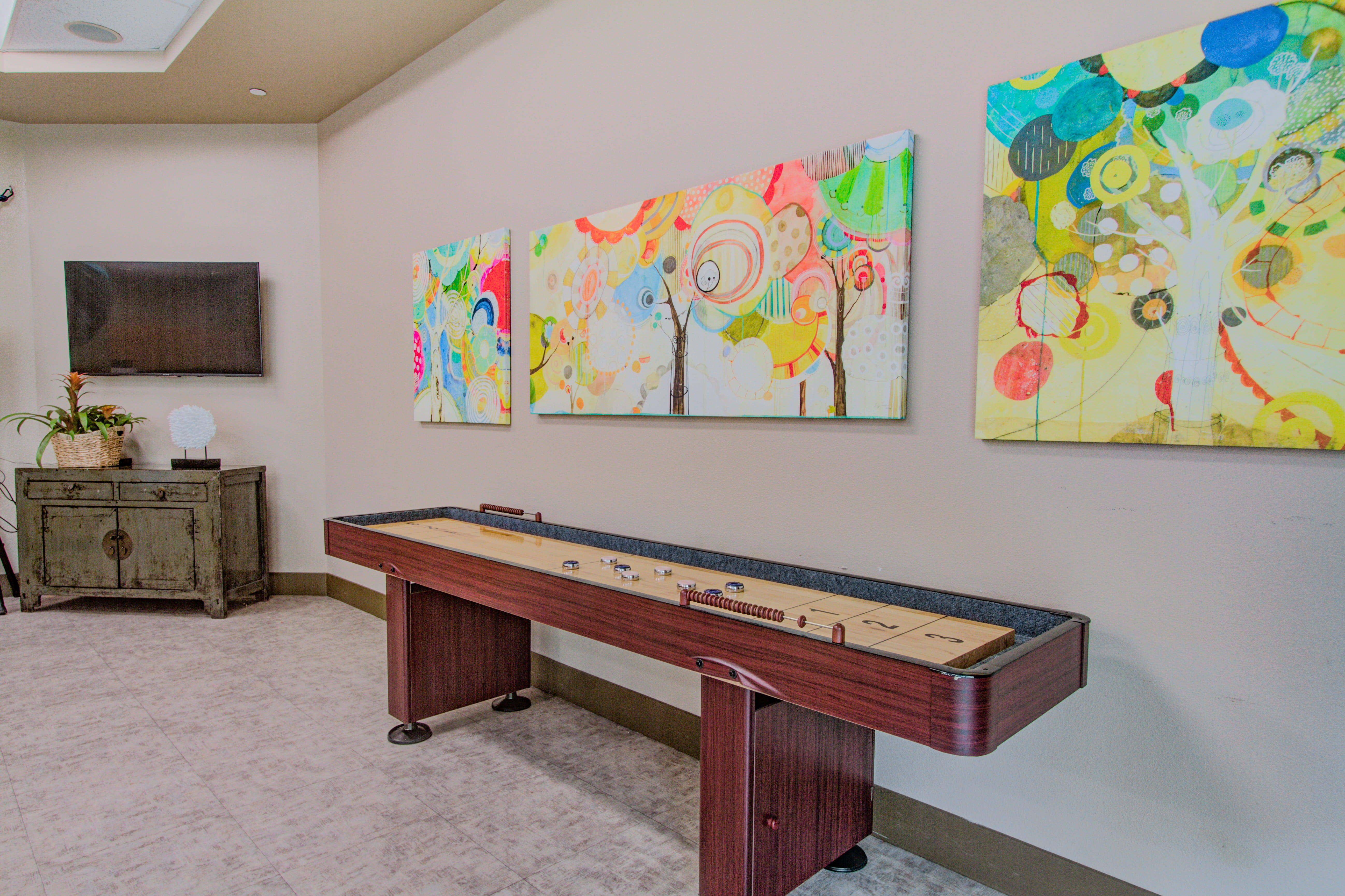 Shuffleboard table and vibrant abstract artwork in a Waikiki activity room.
