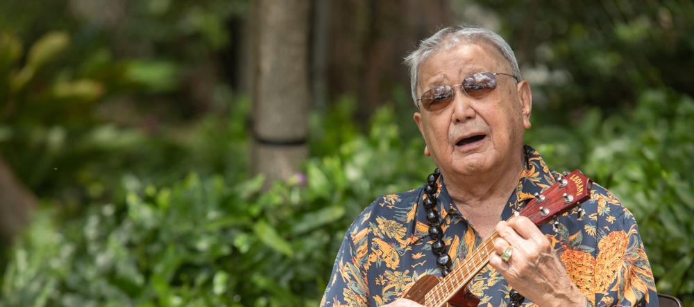 Senior man in an aloha shirt playing the ukulele and singing outdoors at The Plaza Assisted Living.
