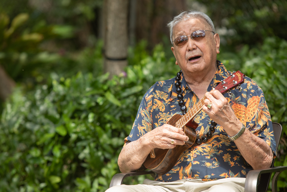Senior man in an aloha shirt playing the ukulele and singing outdoors at The Plaza Assisted Living.